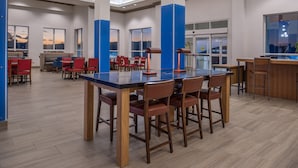 A modern dining area with a long table and multiple chairs, a bar area with stools, and large windows offering views of the cityscape. - Holiday Inn Express Mystic by IHG (Mystic)