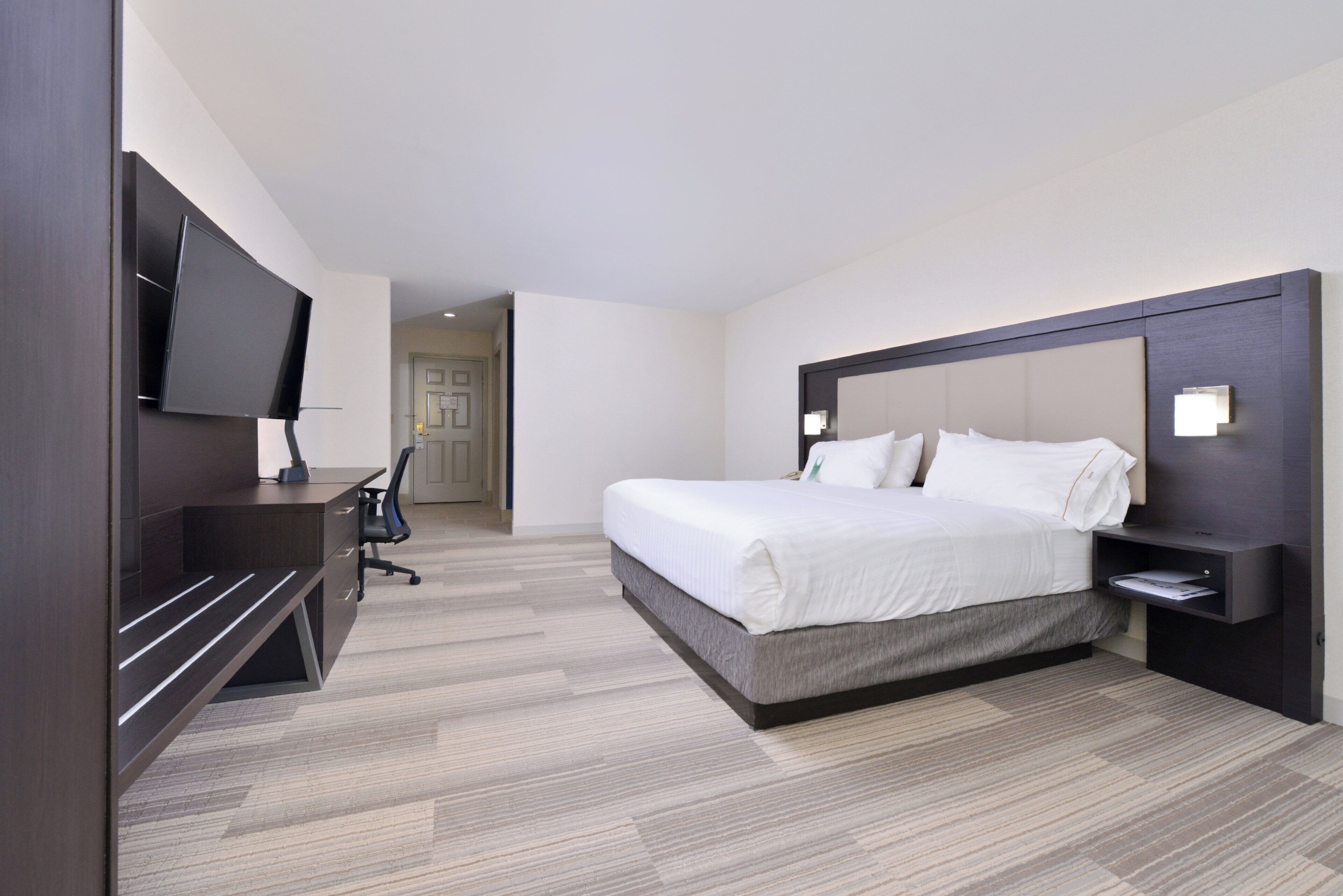 Ein Hotelzimmer mit einem Bett, einem Schreibtisch, einem Sessel, einem Fernseher und einer Tür zu einem weiteren Raum.