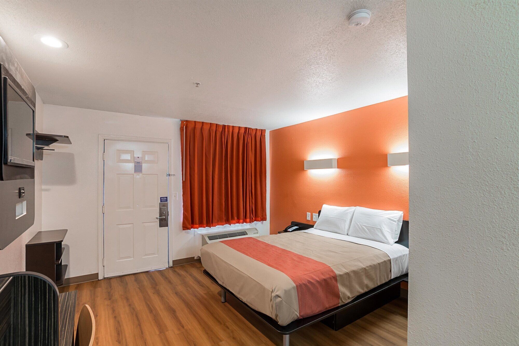 Une chambre d’hôtel avec un lit, un bureau et une fenêtre avec des rideaux orange.