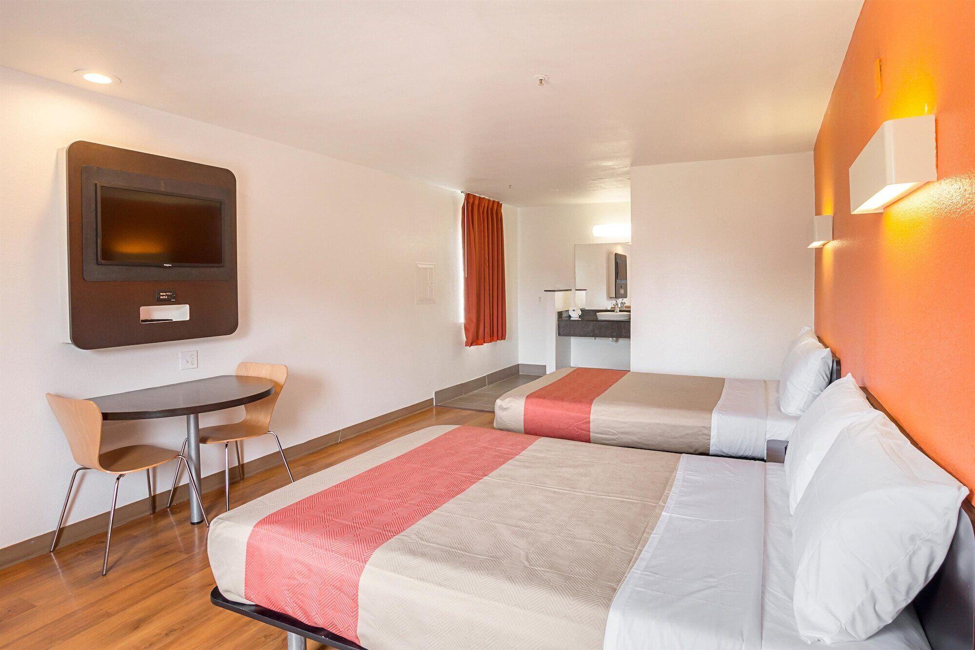 A hotel room with two beds, a desk, a chair, a television, and a bathroom.