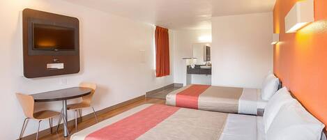 A hotel room with two beds, a desk, a chair, a television, and a bathroom.