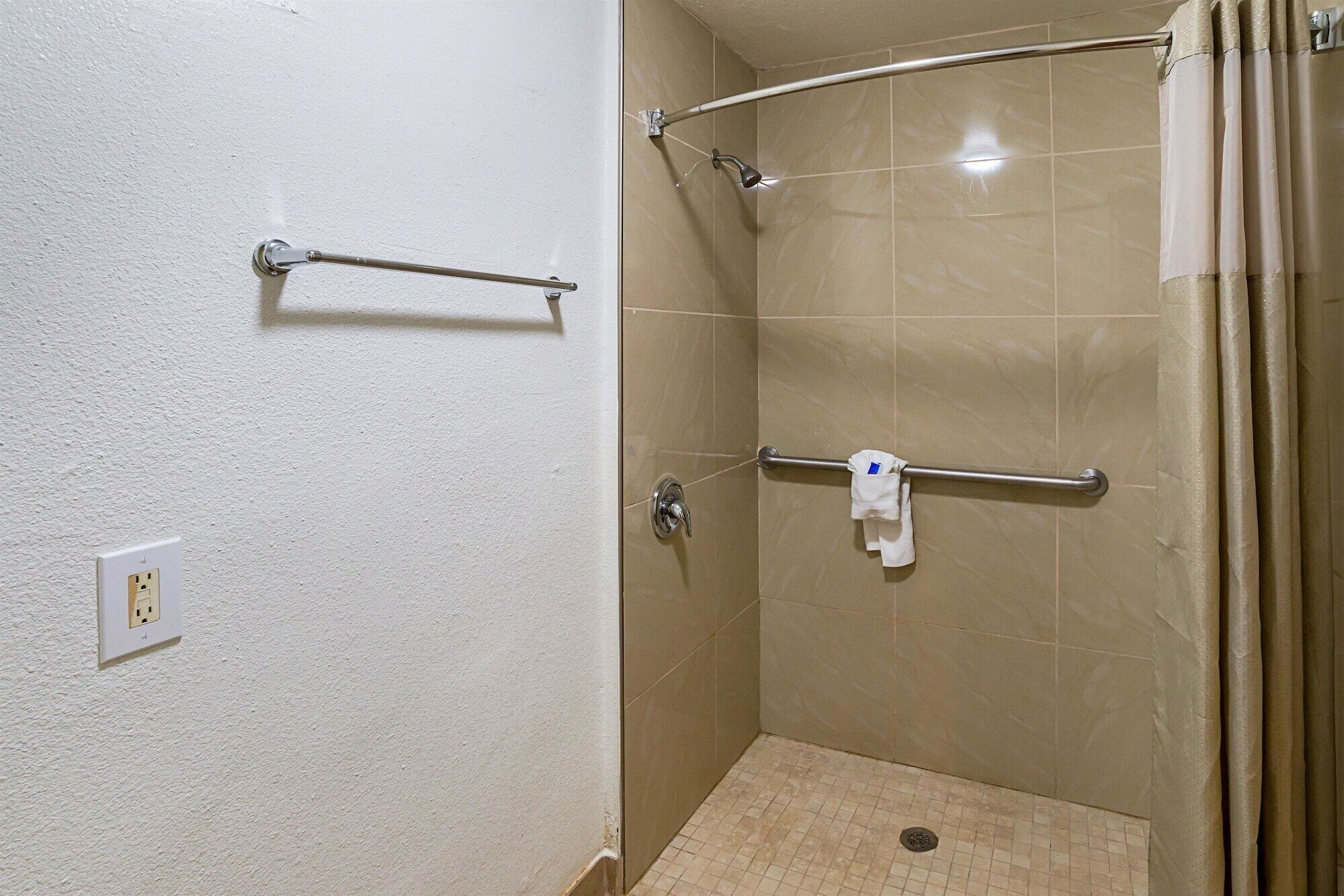 A small, enclosed shower area with a grab bar, a towel rack, and a power outlet on the wall.