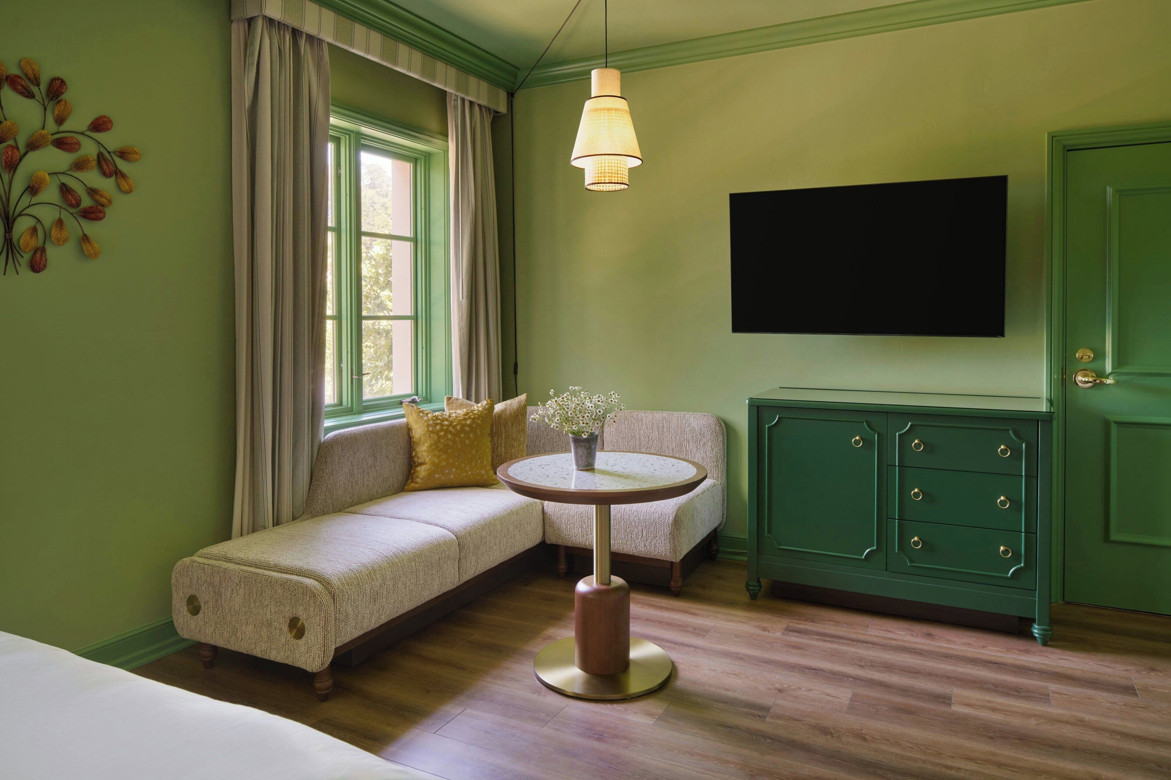 A room with a green wall, a sofa, a round table, a cabinet, and a television.