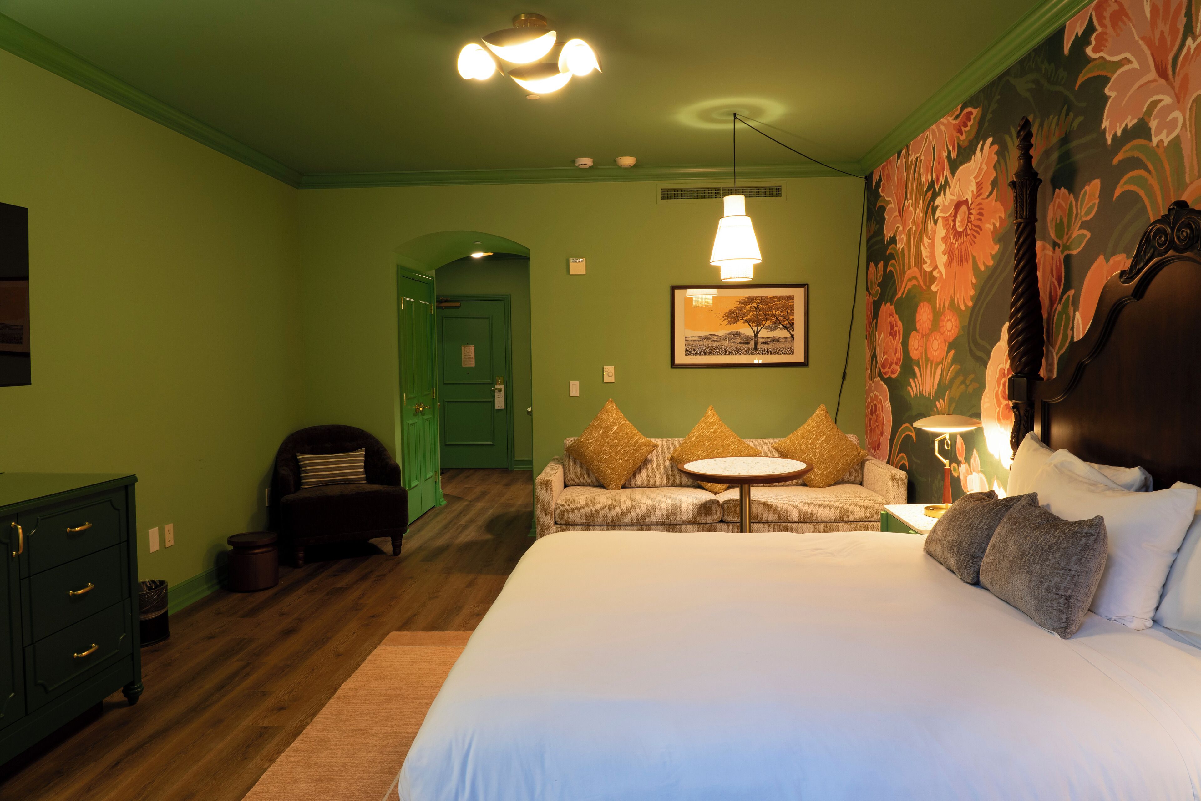 Un dormitorio con una cama grande, un sofá, un aparador y una puerta verde al fondo.