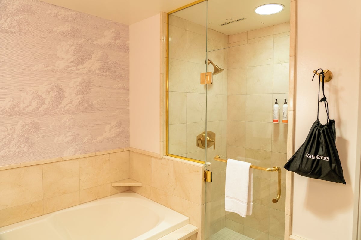 A bathroom with a glass-enclosed shower, a white bathtub, and a towel rack with a black bag hanging on it.