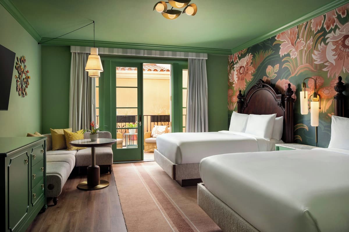 A hotel room with two beds, a sofa, a small table, and a view of the outside.