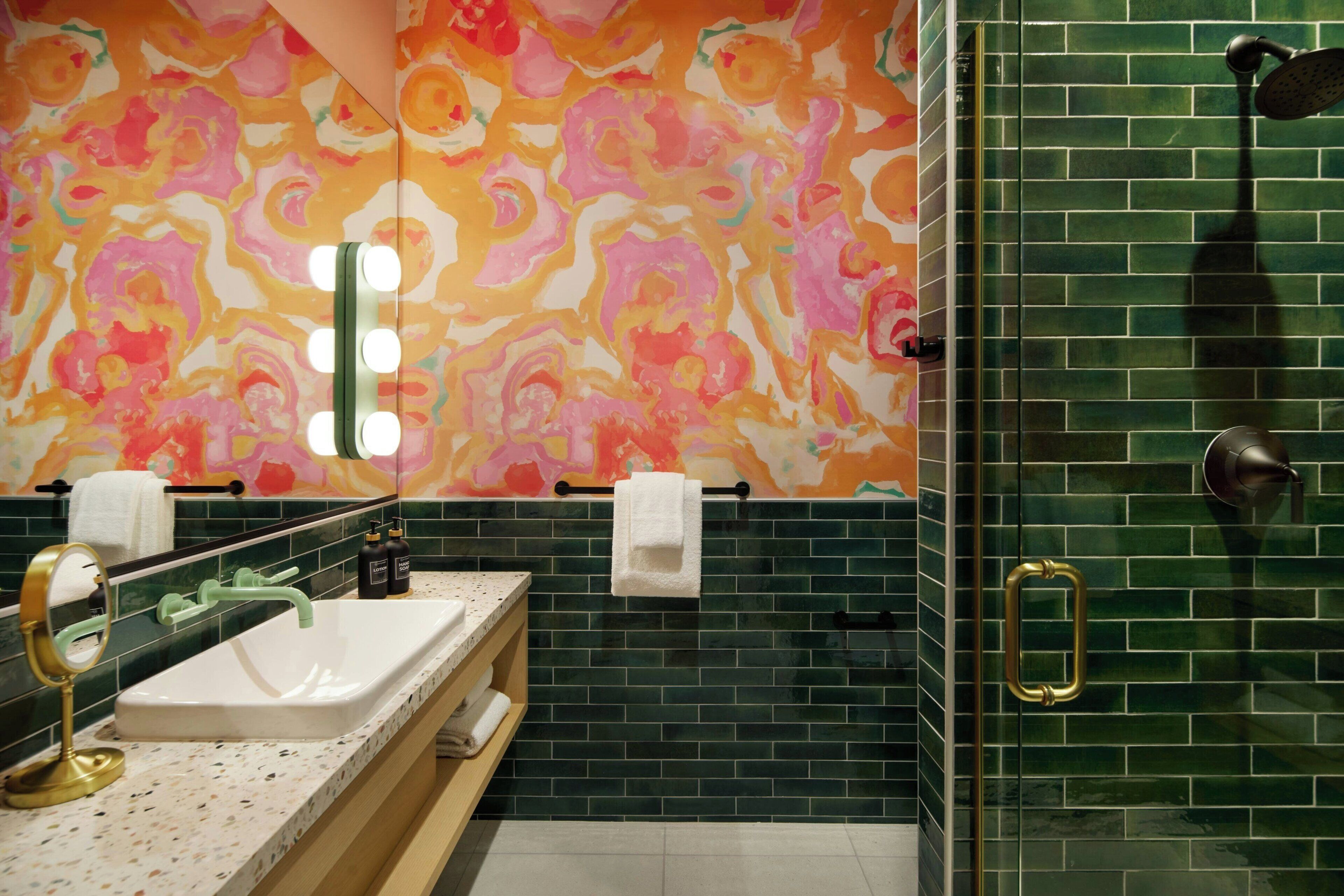 A bathroom with a large mirror, two sinks, a shower, and a colorful wall.