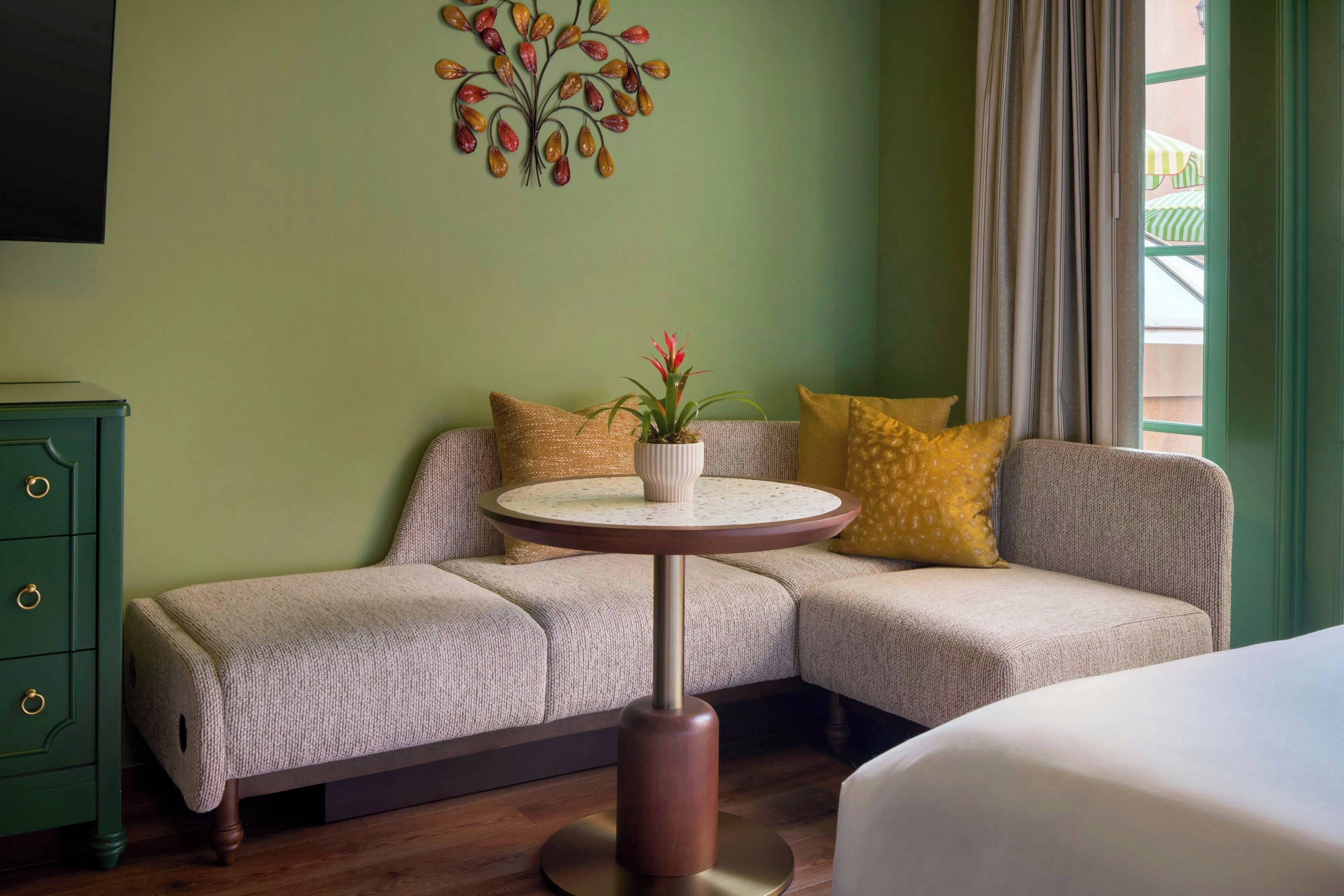 A room with a sofa, a small round table with a plant, a TV on the wall, and a green dresser.