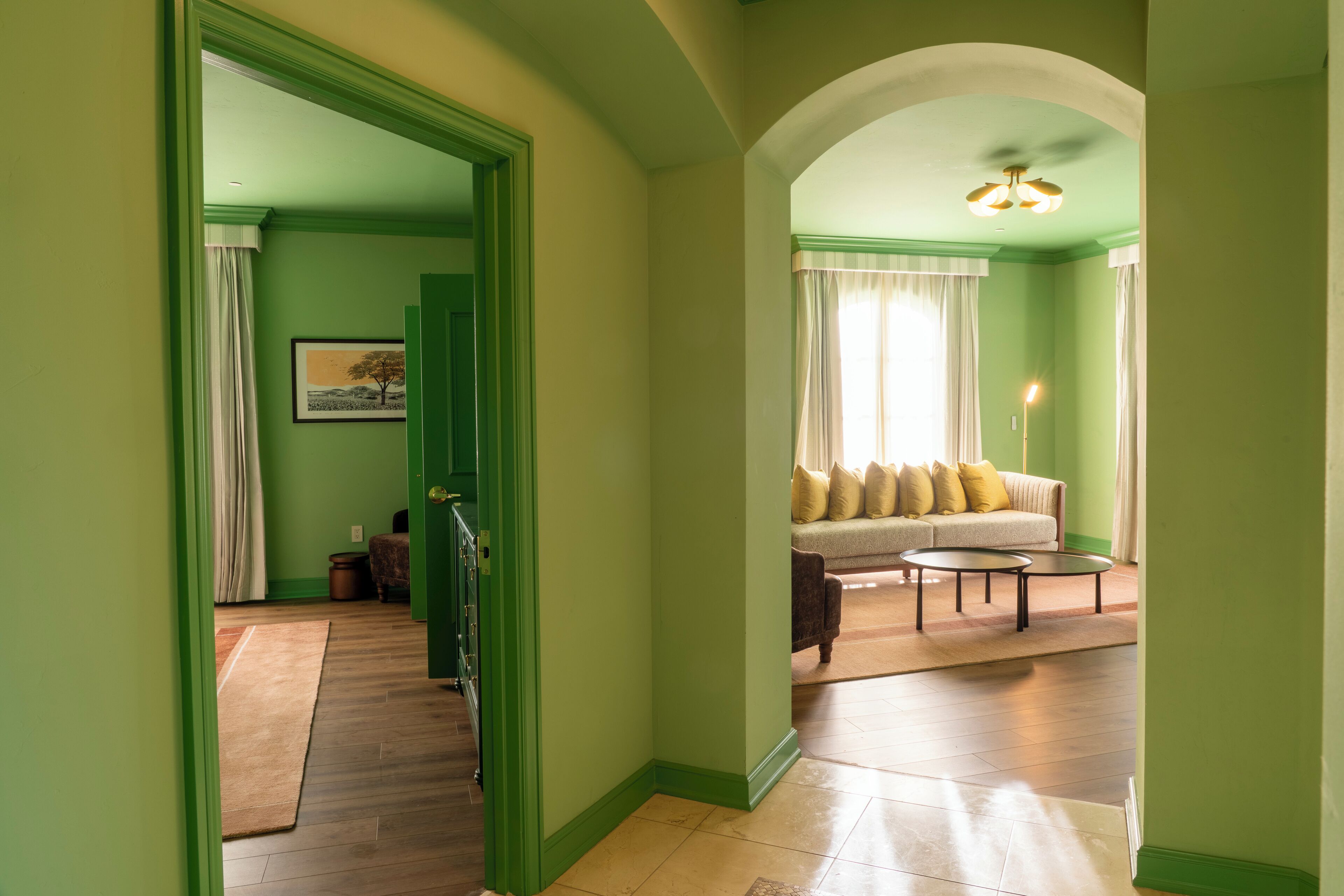 A hallway with green walls and wooden flooring leading to a living room with a sofa and a coffee table.