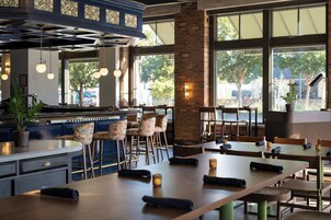 A restaurant interior with high ceilings, exposed brick walls, and large windows offering views of the outdoors.