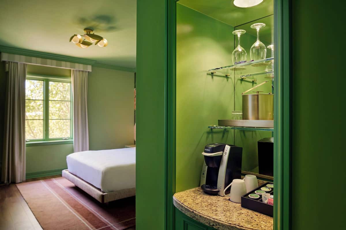 A hotel room with a bed, a coffee maker, a mirror, and a window with curtains.