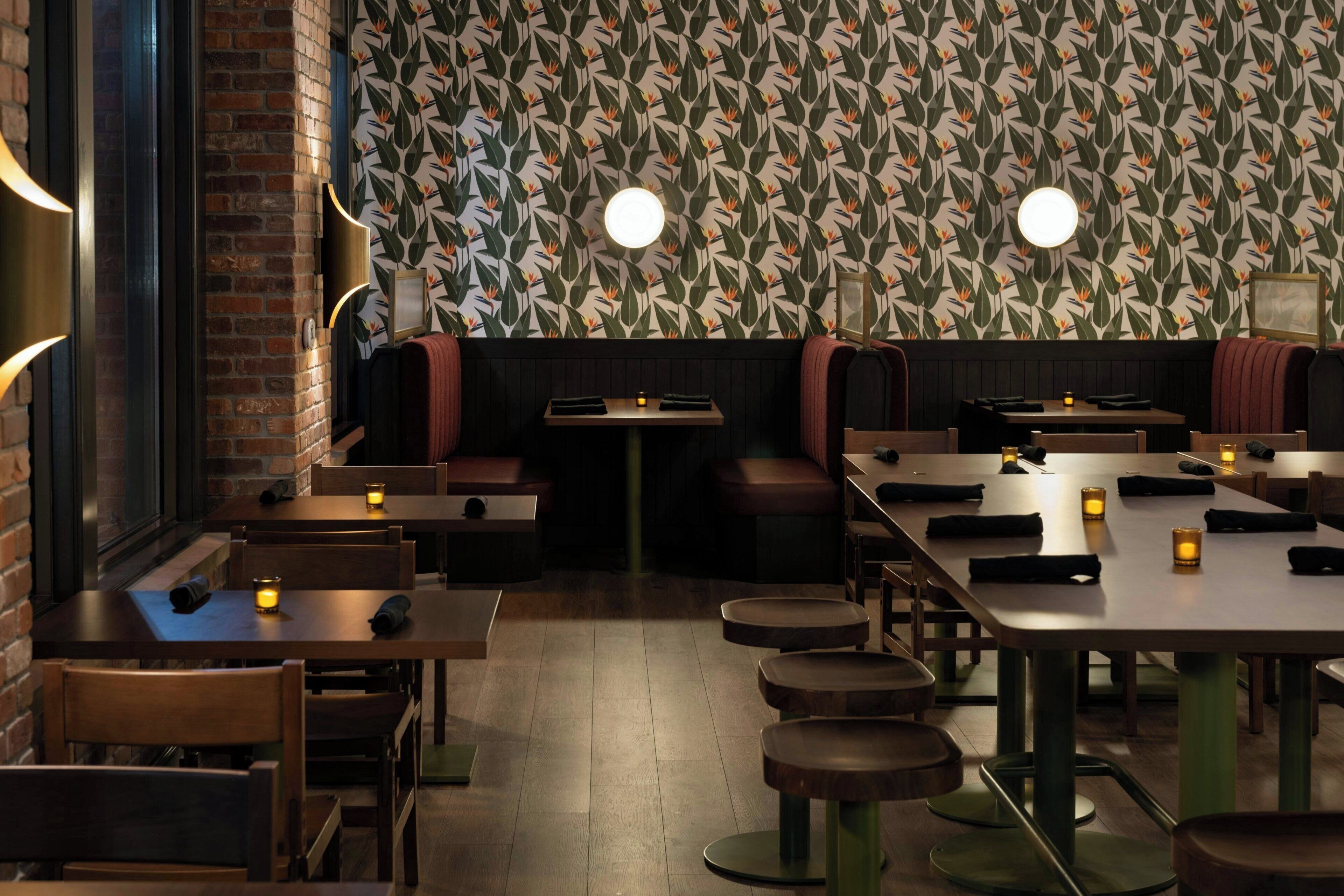 A restaurant interior with brick walls, patterned wallpaper, and round tables with stools.