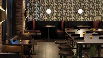 A restaurant interior with brick walls, patterned wallpaper, and round tables with stools.