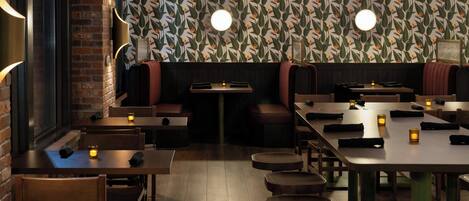 A restaurant interior with brick walls, patterned wallpaper, and round tables with stools.