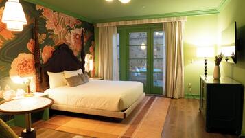 A neatly arranged bedroom with a bed, bedside table, lamp, and a view of the outside through a glass door.