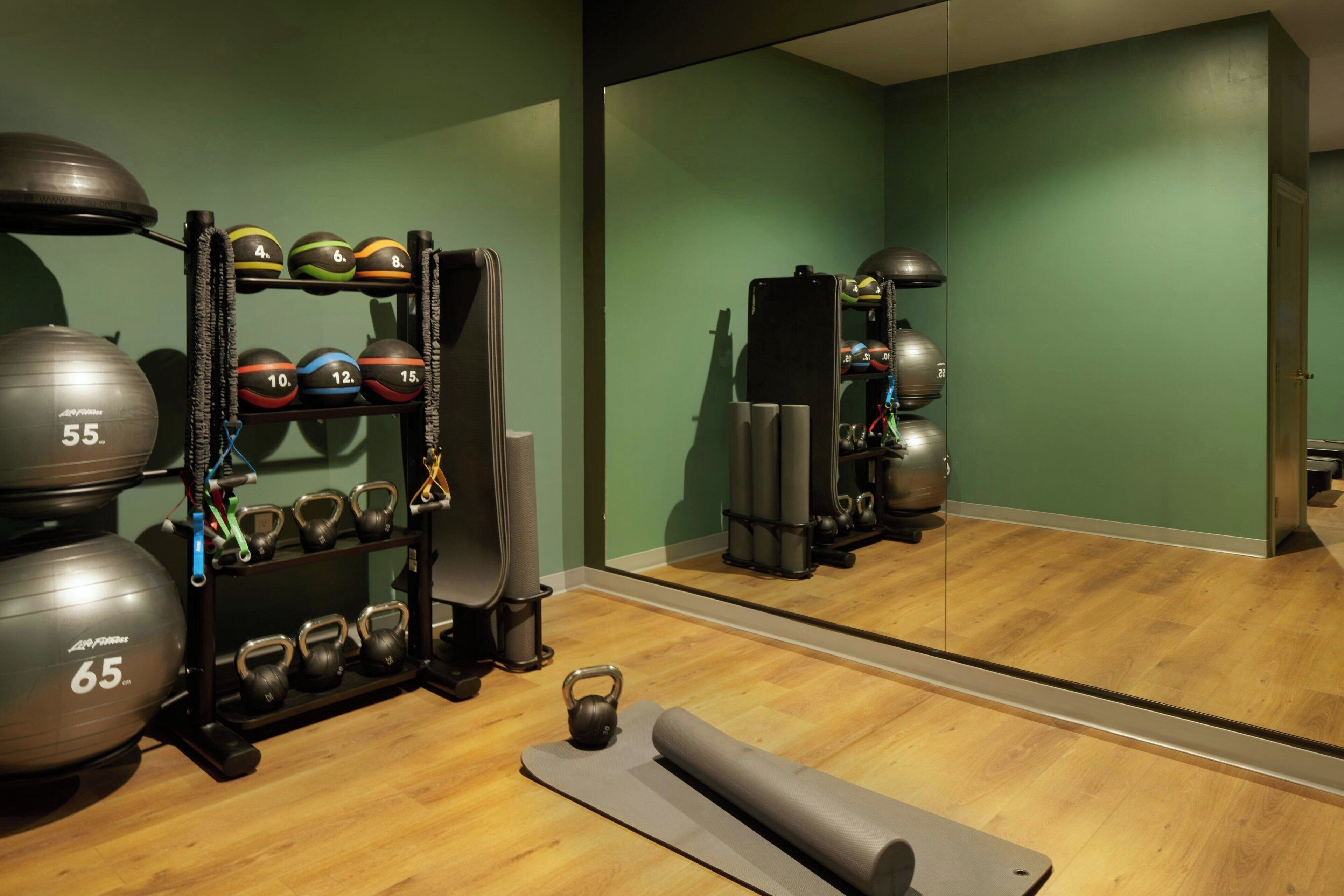 A gym with exercise equipment, a mirror, and a wooden floor.