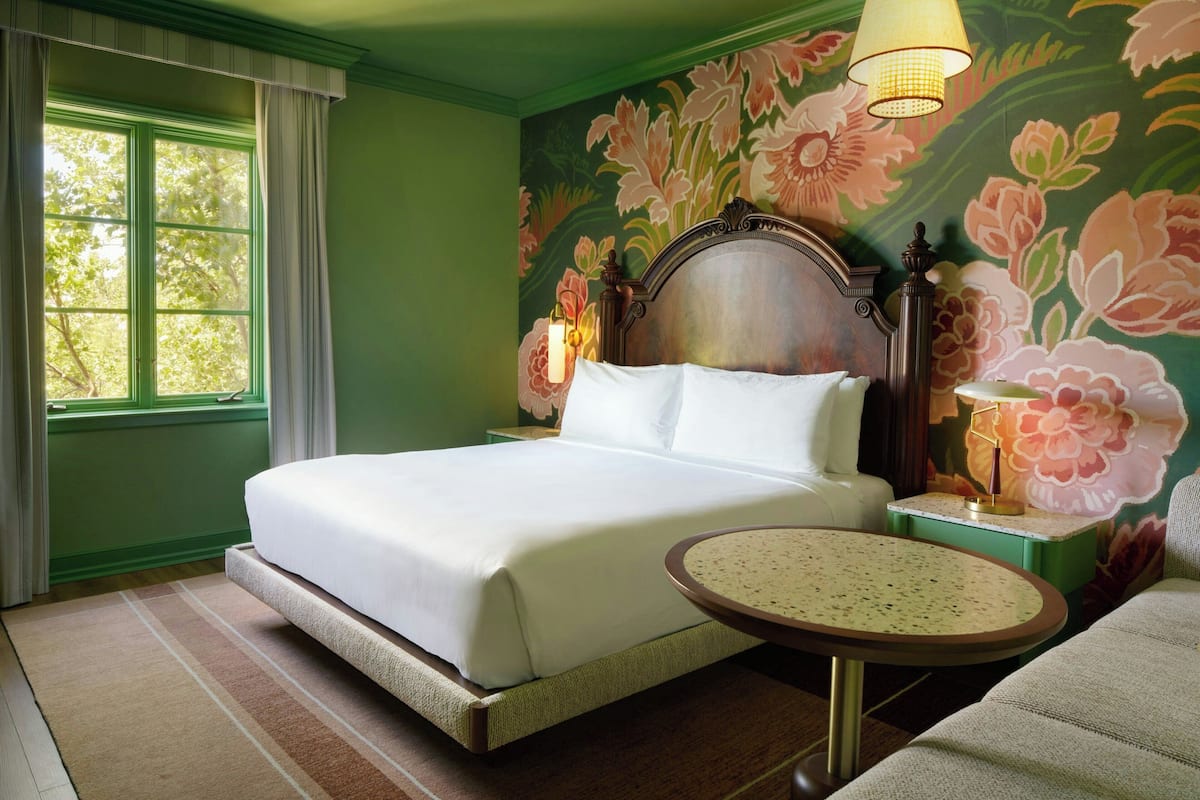 A bed with a headboard, a round table, a lamp, and a floral wall mural.