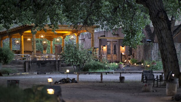A rustic wooden building with a covered patio area, outdoor seating, and a pond.