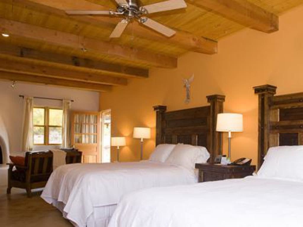 A hotel room with two beds, wooden headboards, a ceiling fan, and a window with curtains.