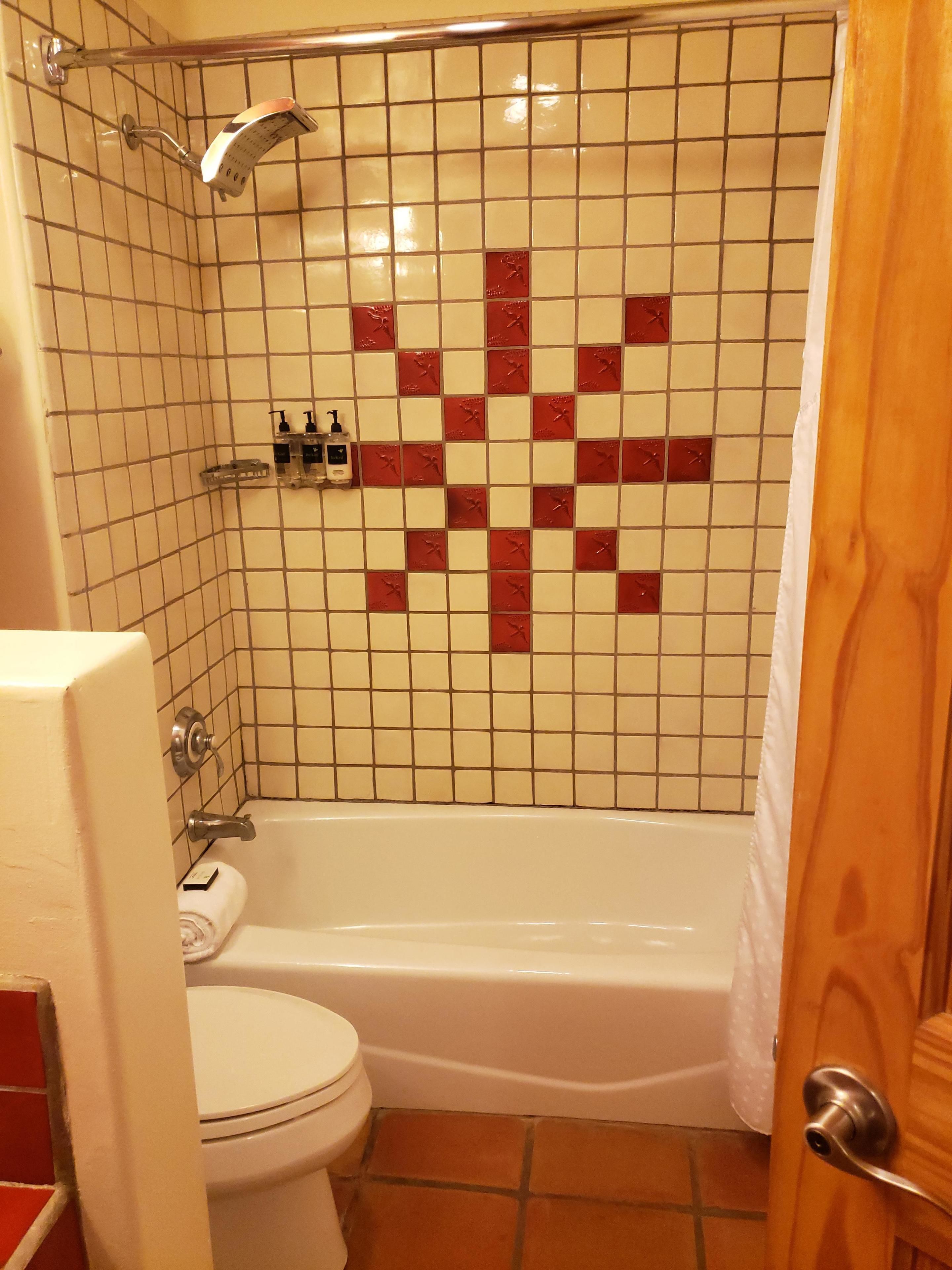 Ein Badezimmer mit einer weißen Badewanne, einer Toilette und einer Dusche mit rotem Mosaikfliesenmuster.