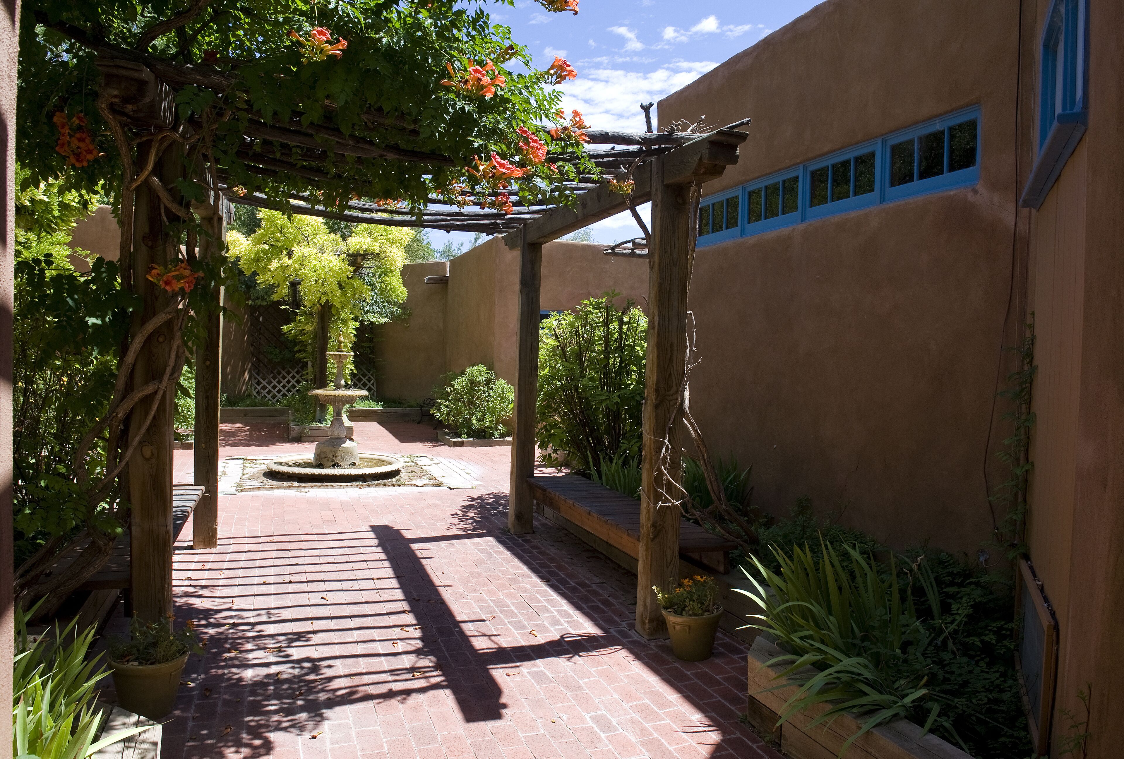 A courtyard with a pergola, a fountain, and potted plants.