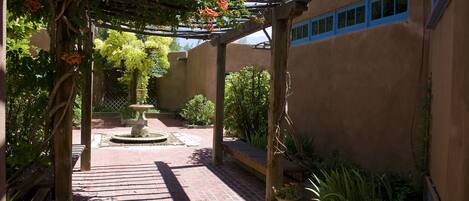 A courtyard with a pergola, a fountain, and potted plants.