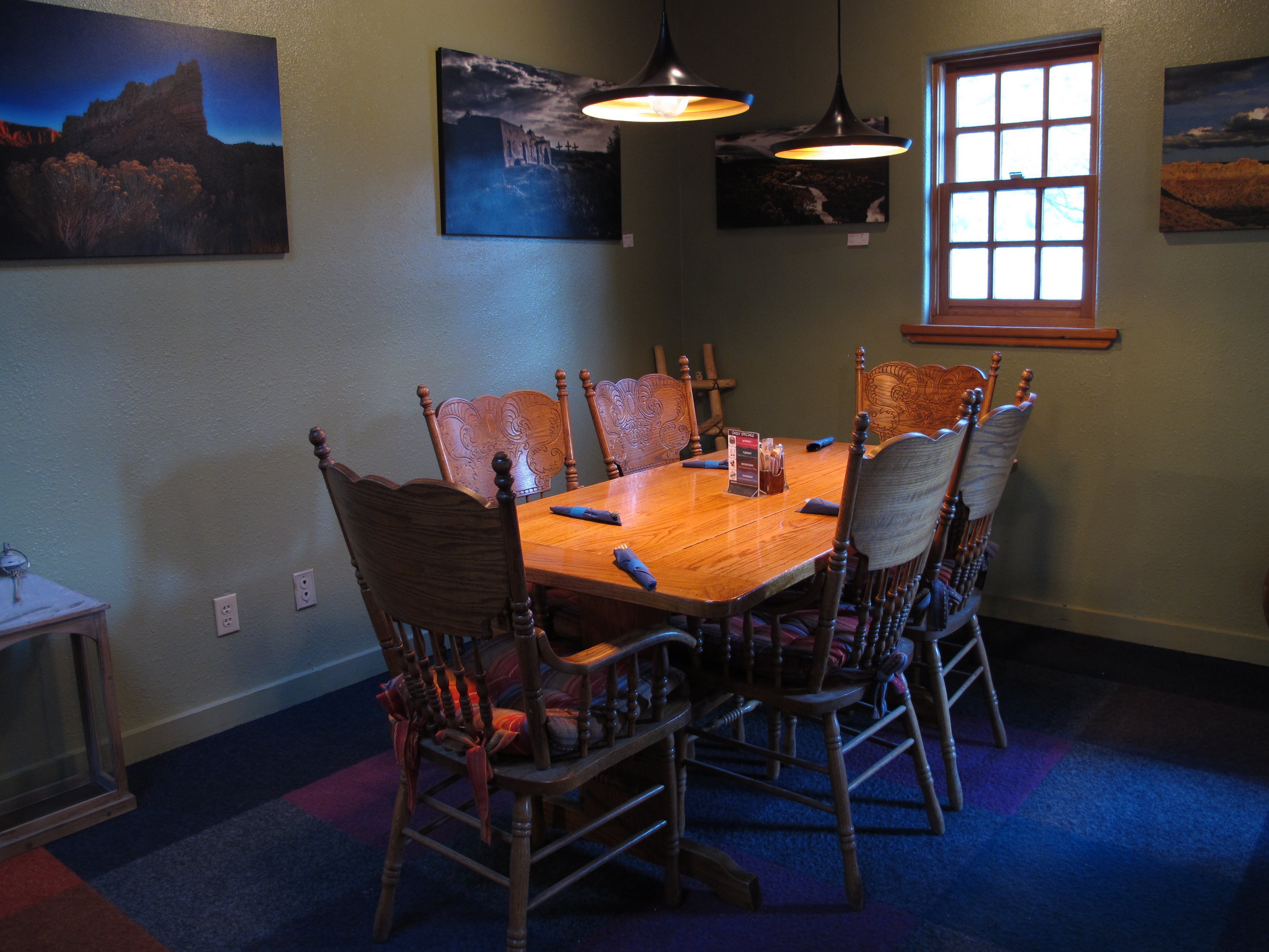 Un comedor con mesa y sillas de madera, lámparas colgantes y obras de arte en las paredes.