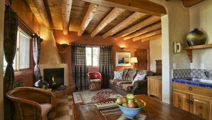A cozy living room with a fireplace, wooden furniture, and a dining area with a bowl of fruit.
