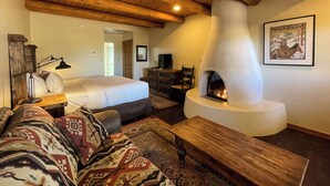 A cozy room with a bed, a sofa, a wooden bench, a fireplace, a dresser, and a framed picture on the wall.