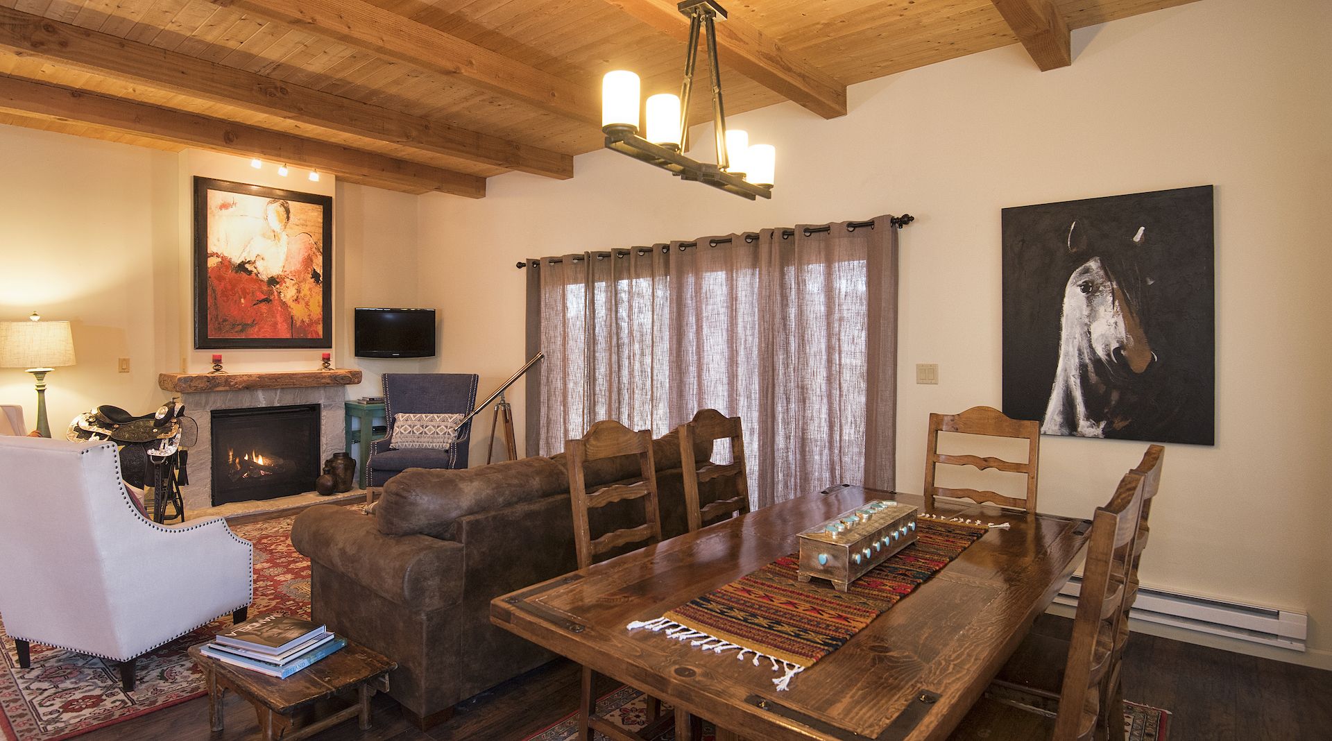 A cozy living room with a fireplace, a dining table, and a large painting on the wall.