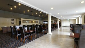 Un comedor amplio con varias mesas y sillas, una barra con caja registradora y una alfombra estampada.