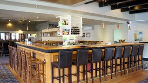 Una zona de bar con una barra alargada, varios taburetes y una estantería para vinos.
