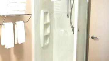 A glass-enclosed shower room with a white door, a towel rack with towels, and a shelf unit.