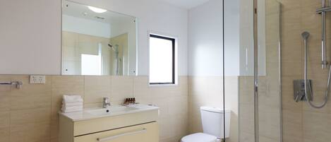 Un baño moderno con ducha envuelta en vidrio, inodoro y tocador con espejo y lavamanos.