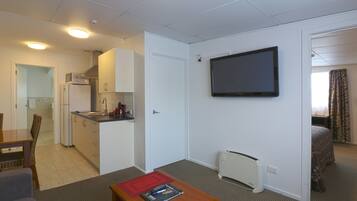 A compact hotel room with a kitchenette, a flat-screen TV, a dining area, and a bed.