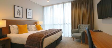Habitación de hotel con una cama grande, un escritorio, una silla, un televisor y dos cuadros en la pared.