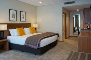 Quarto de hotel com cama, mesas de cabeceira, escrivaninha e espelho.