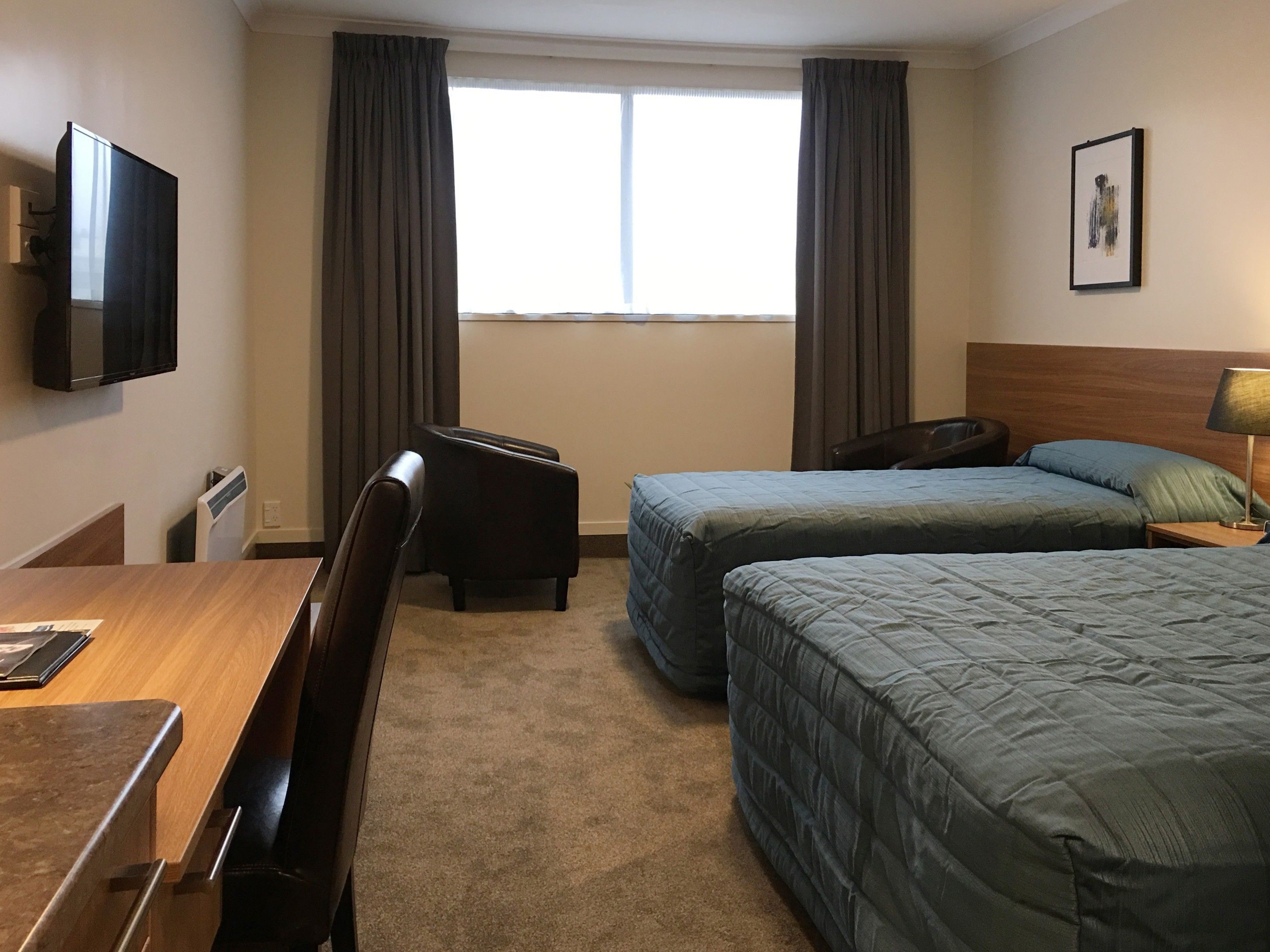 A hotel room with two beds, a desk, a chair, a TV, and a window with curtains.