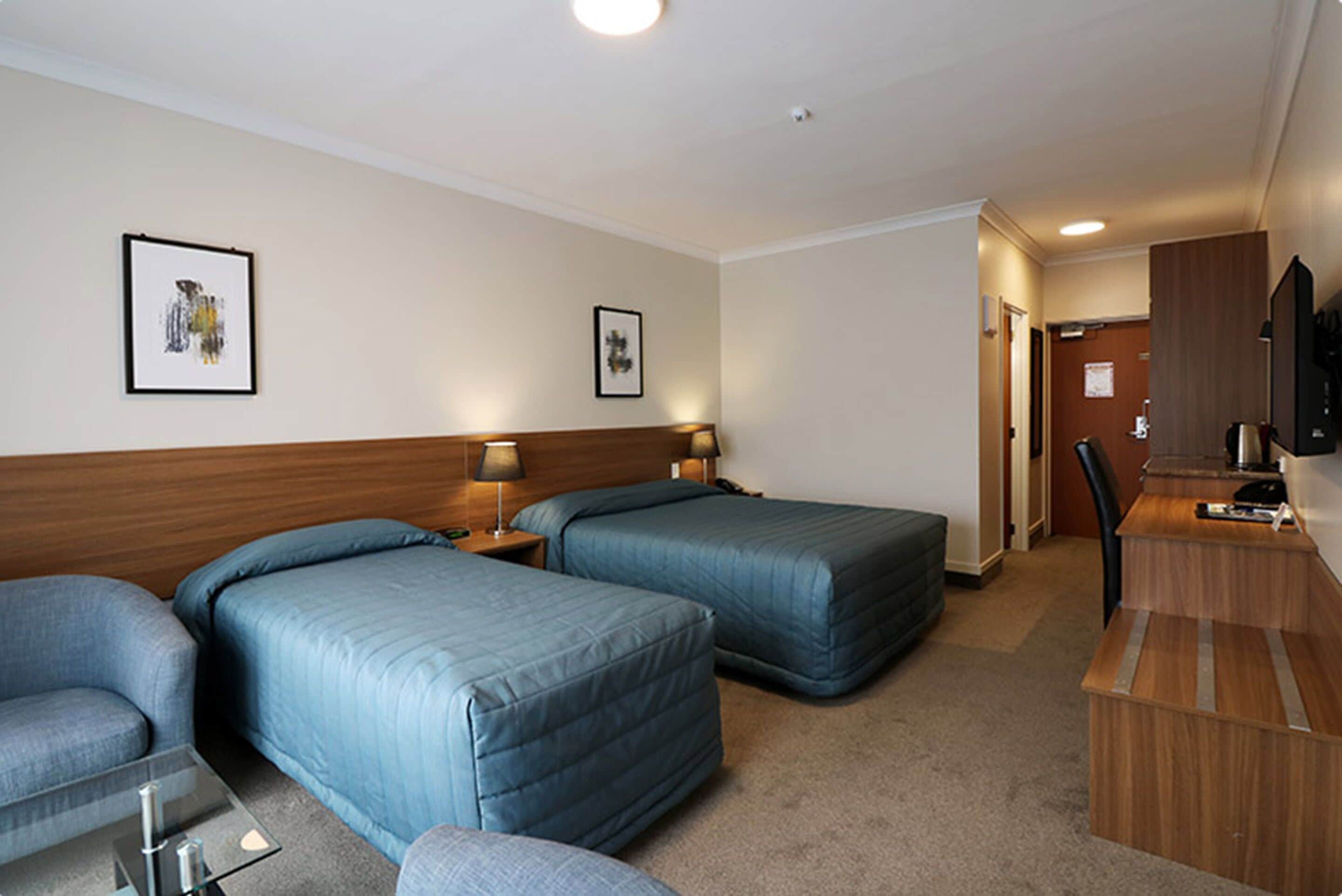 A hotel room with two single beds, a desk, a chair, and a television.