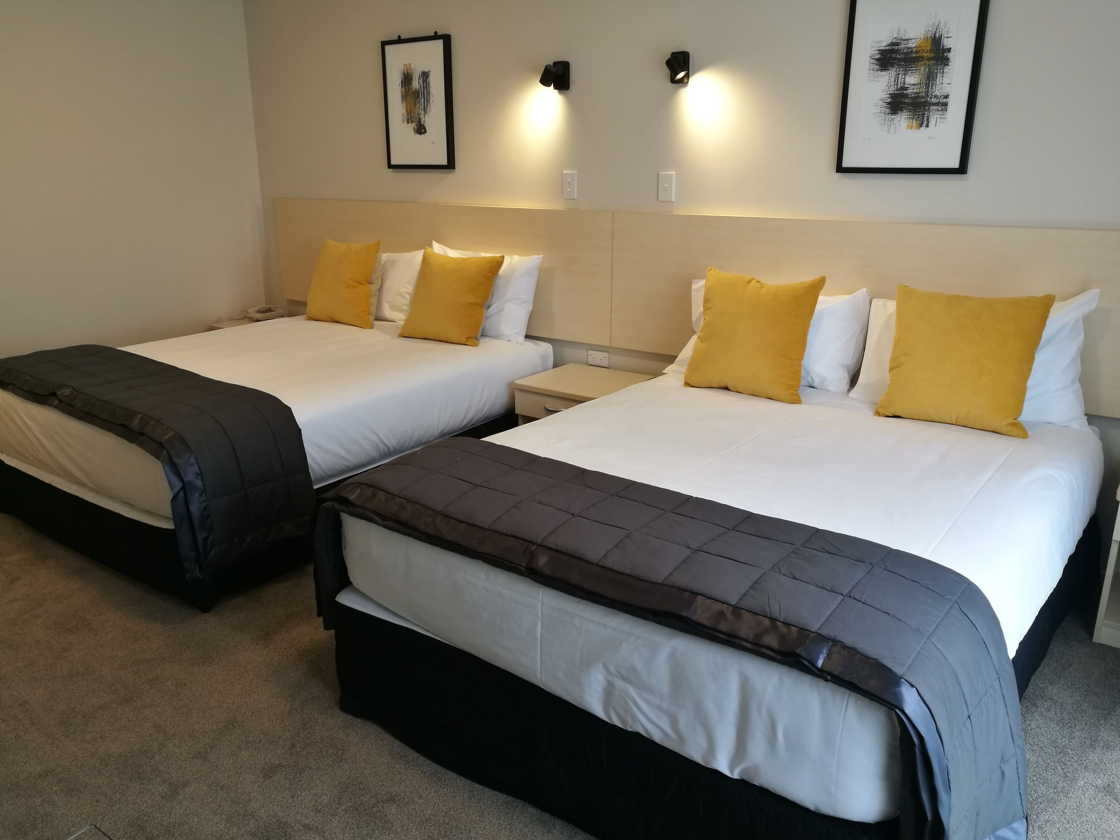 A hotel room with two beds, each with a black and white quilted bedspread and yellow pillows.