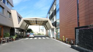Un edificio moderno con acceso cubierto, zona de estacionamiento y asientos al aire libre.