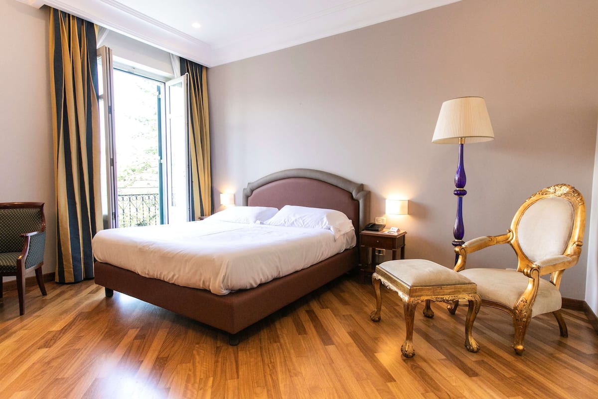 A hotel room with a large bed, a chair, a small table, and a lamp.