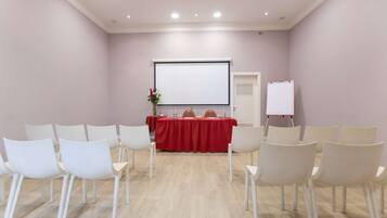 Una sala conferenze con un tavolo rosso, sedie bianche, uno schermo per proiettore e una lavagna a fogli mobili.