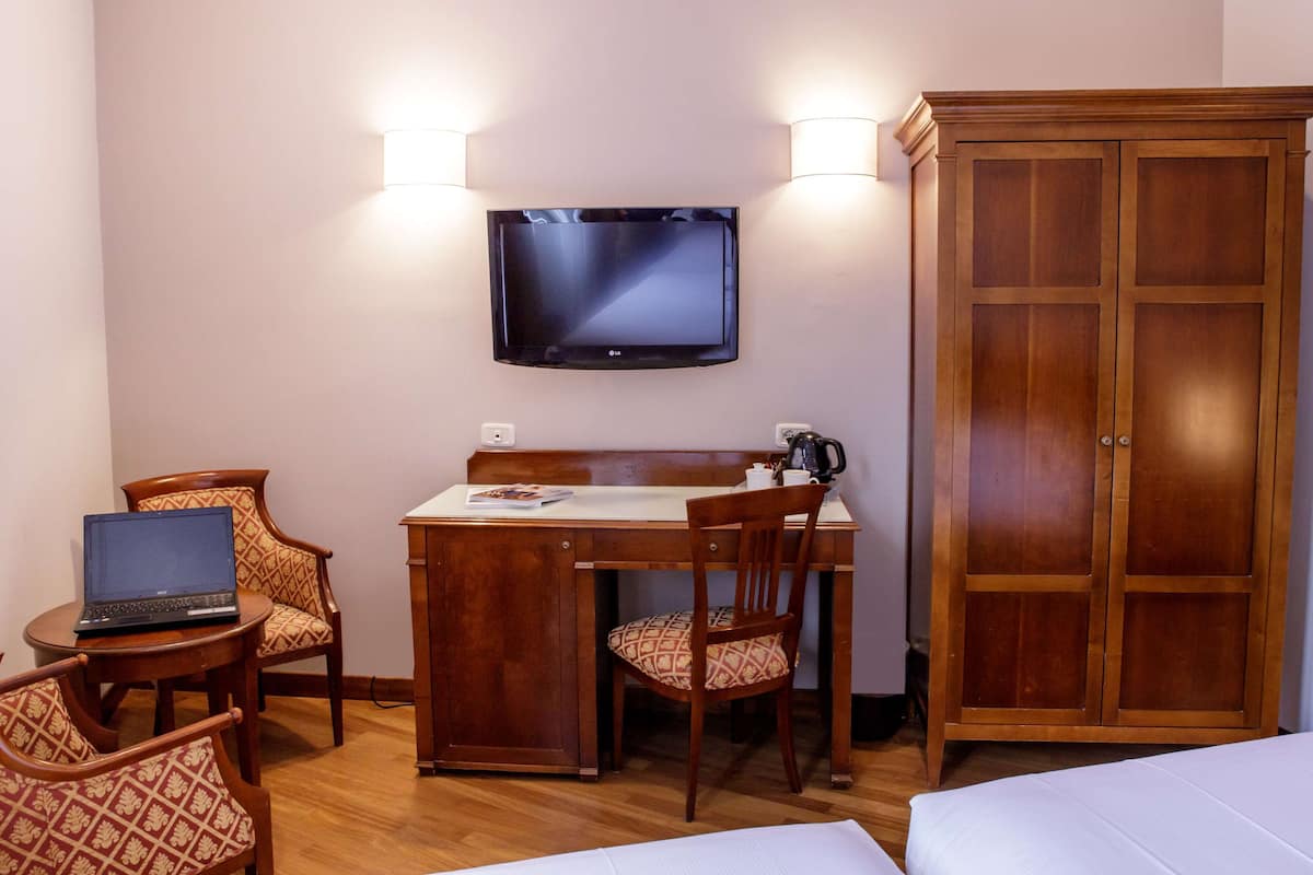 A hotel room with a wooden desk, two chairs, a laptop, a television, and a wardrobe.