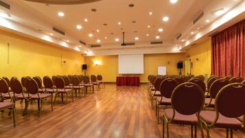 Un salón de conferencias con filas de sillas, una pantalla de proyector y un atril.