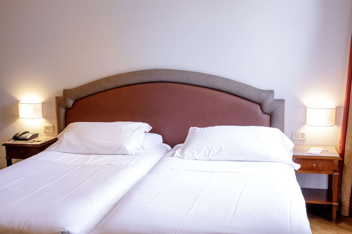 A double bed with white linens, a wooden headboard, bedside tables with lamps, and a telephone on one of the tables.