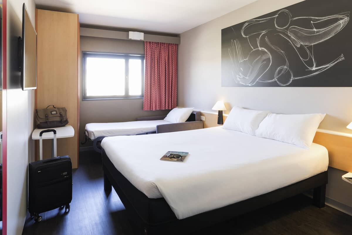 Une chambre d’hôtel avec deux lits, un bureau, une valise et un grand tableau abstrait accroché au mur.