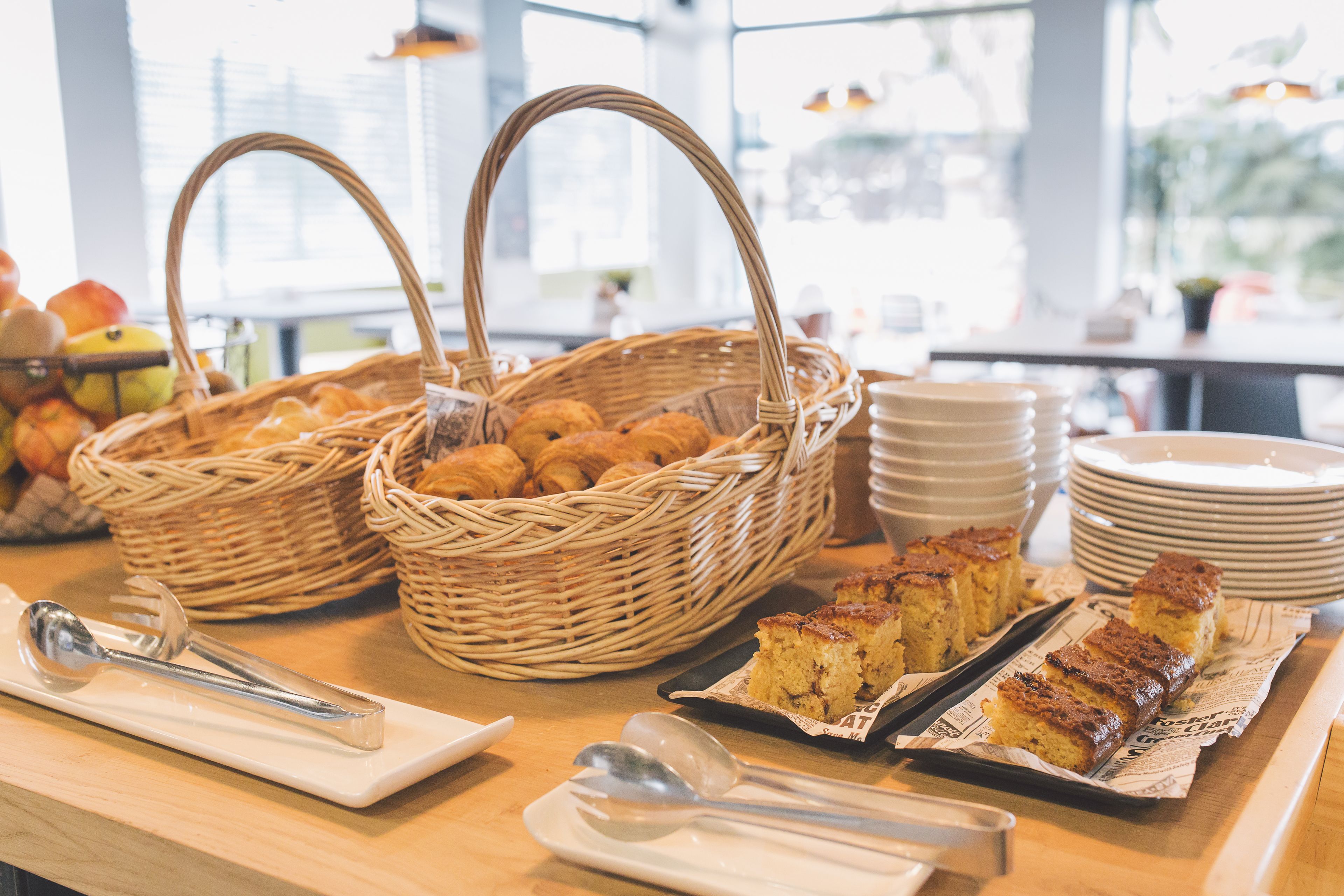 Un bufé de desayuno con cestas de mimbre, platos y utensilios para servir.