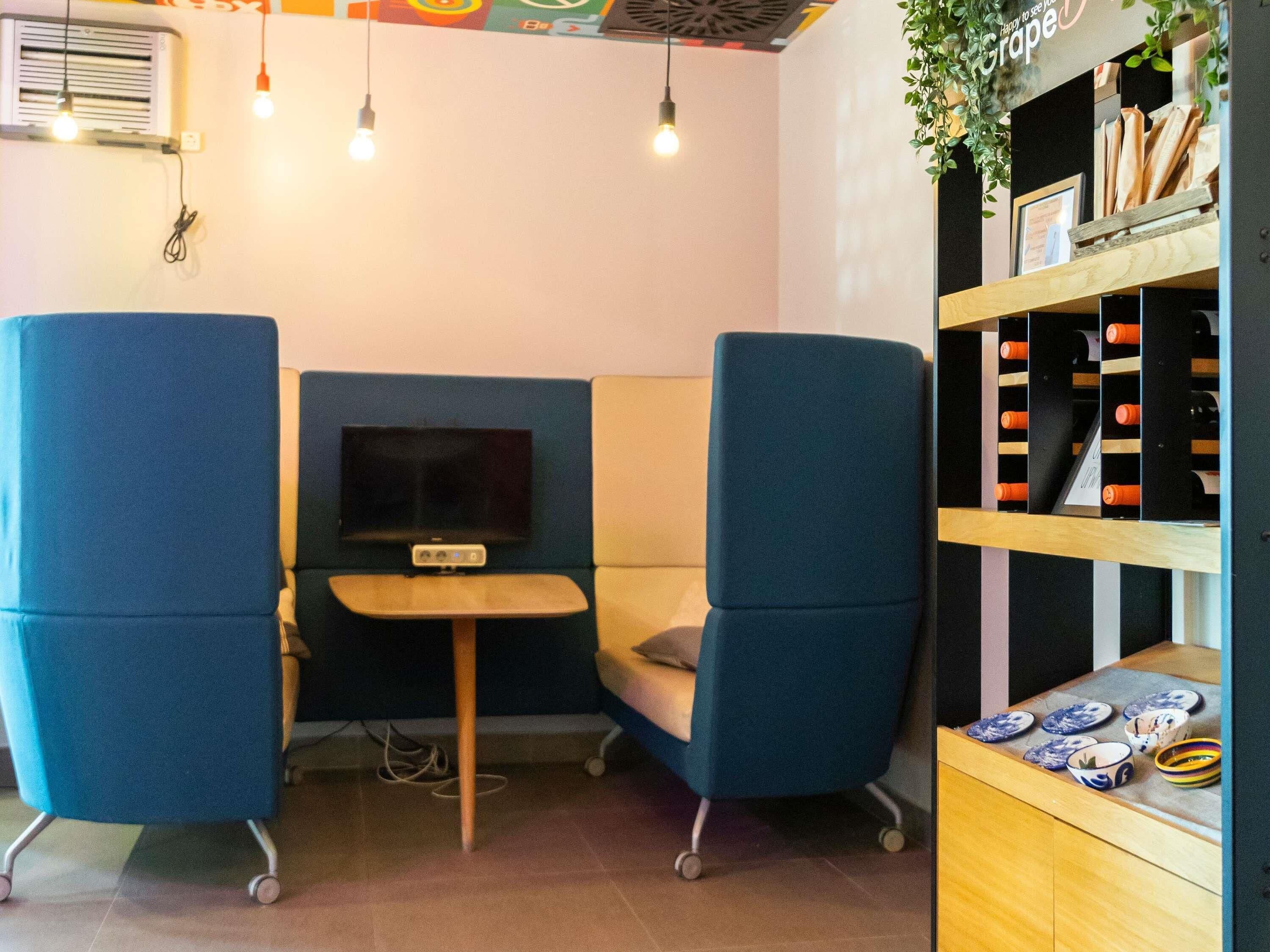 A seating area with two blue chairs, a small table, a television, and a wine rack with bottles.
