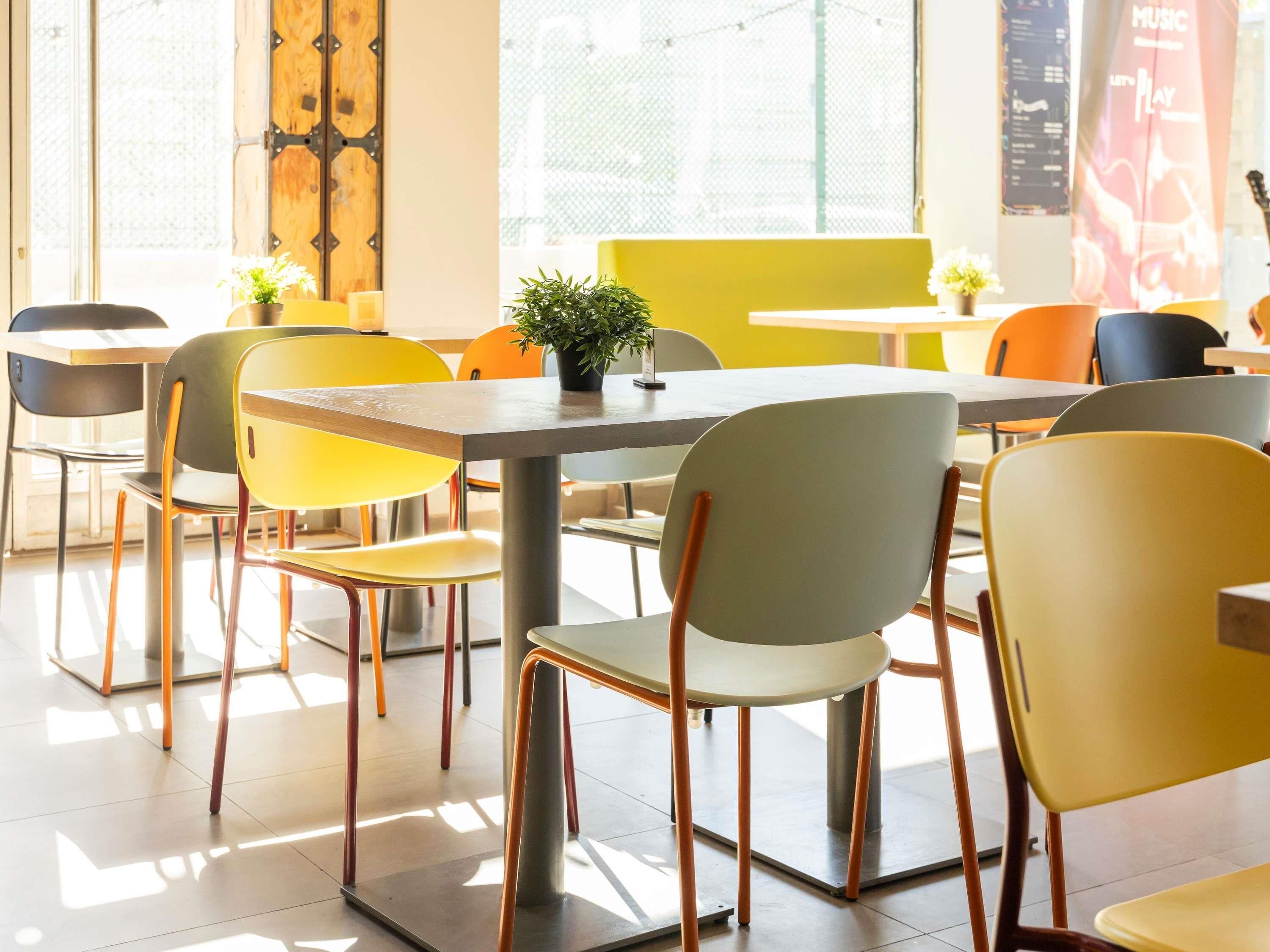 Un comedor moderno con mesas y sillas, ventanas amplias y una puerta visible con detalles metálicos.